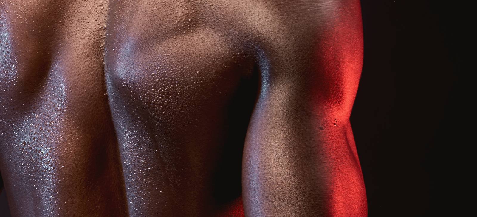Detalle de una espalda con gotas de sudor, iluminada de lado por luz roja