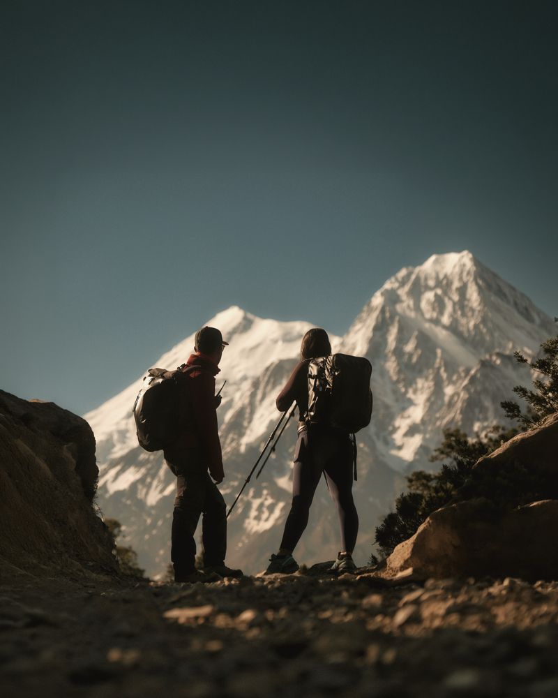 Dos senderistas a contraluz frente a una montaña nevada al anochecer
